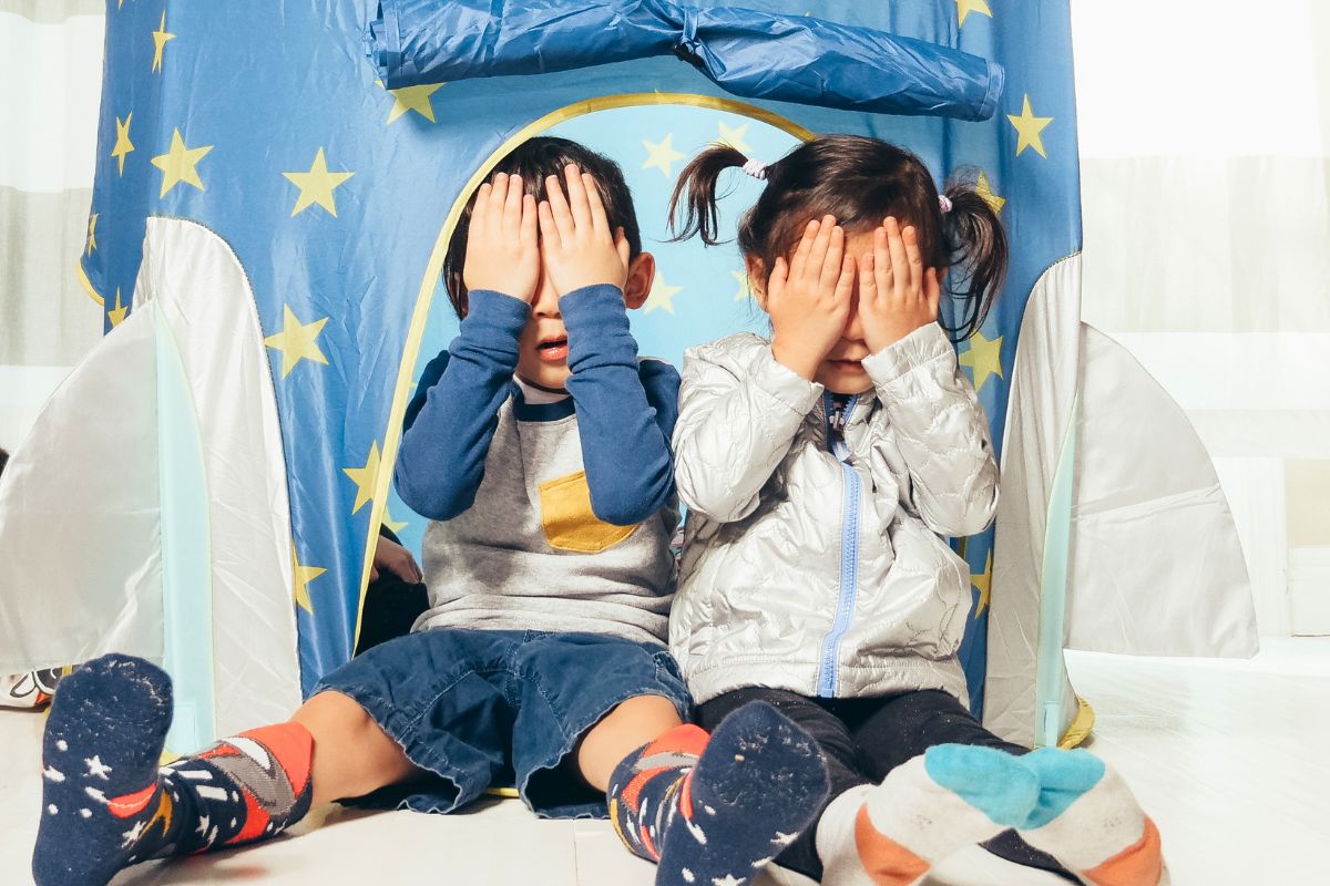 Kids playing hide and seek inside play tent during indoor family activity.