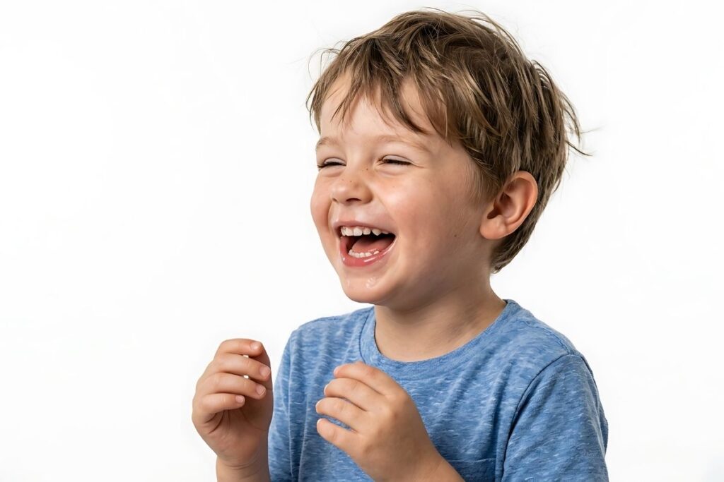 Young boy in a blue T-shirt laughing with his mouth open and hands raised against a white background.