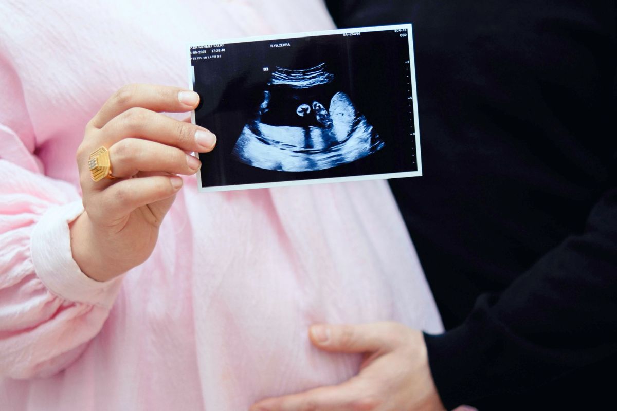 Pregnant woman holding an ultrasound photo while touching the belly, showing excitement for the baby.
