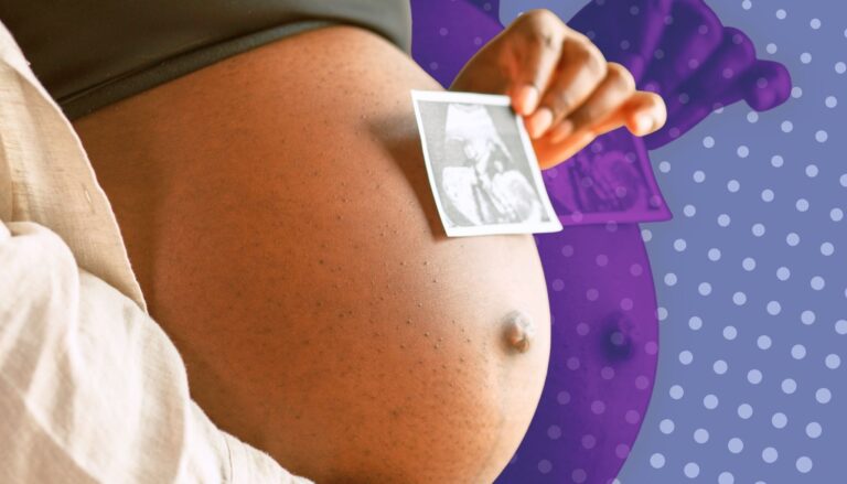 Pregnant woman holding a small ultrasound photo against her belly, showing early baby imaging.