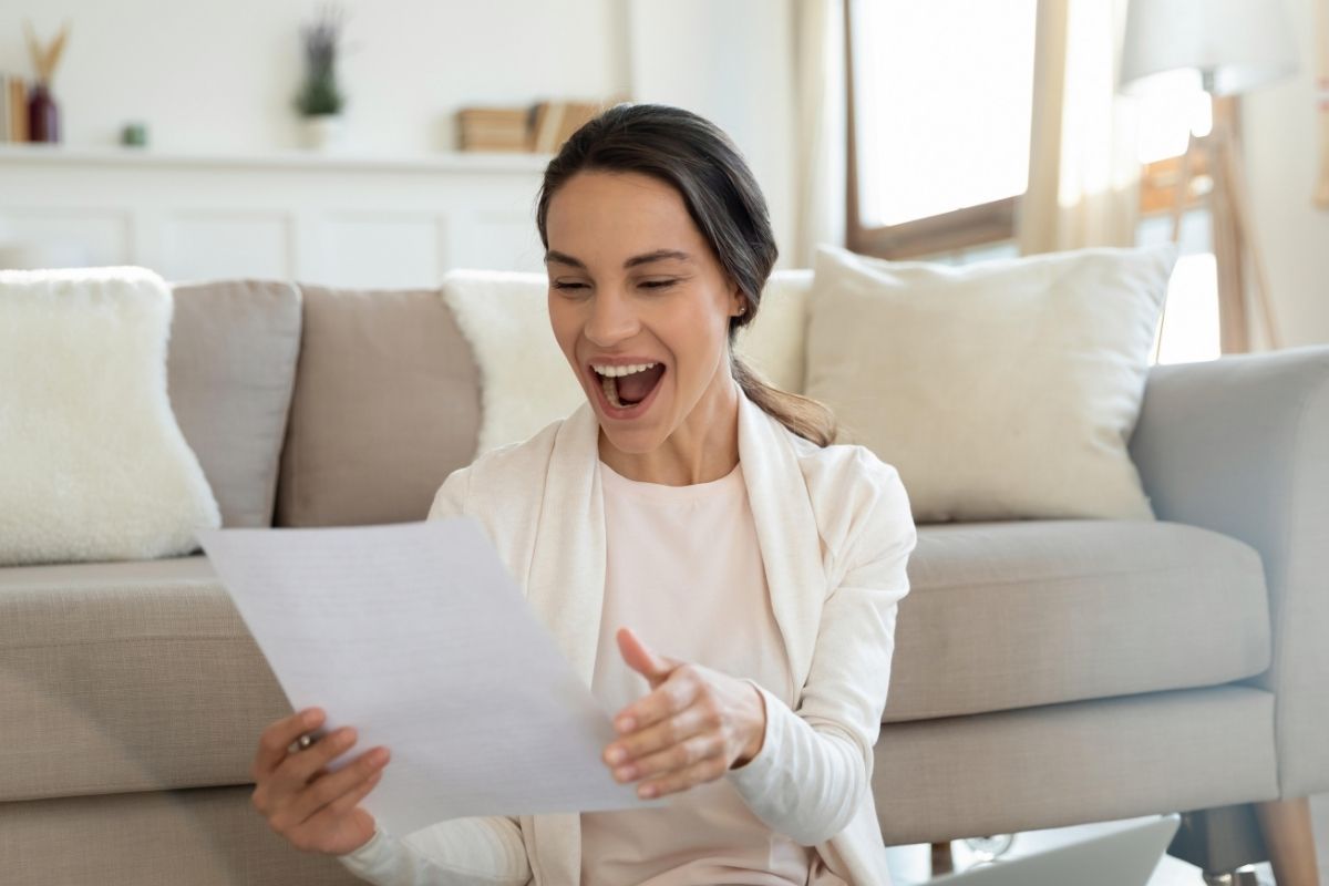 Smiling woman reading a letter or card while sitting at home.