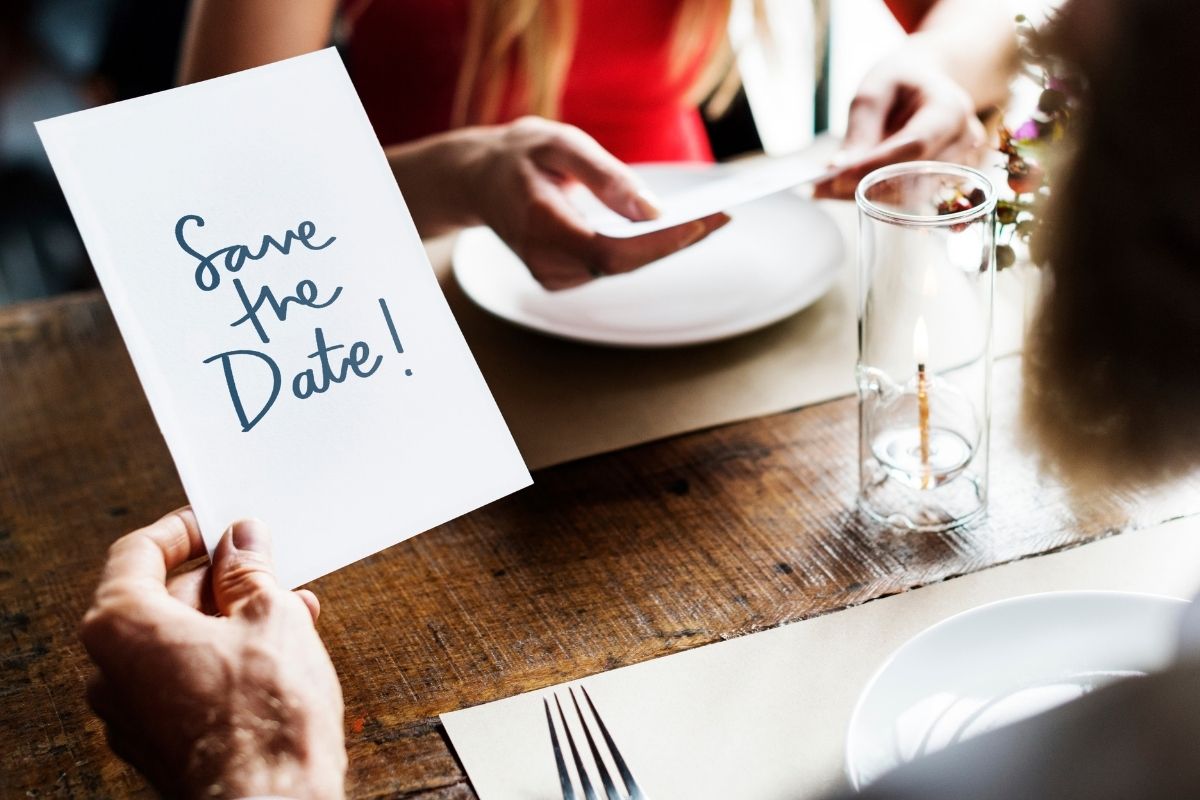 Person holding a “Save the Date” card while sitting at a table.