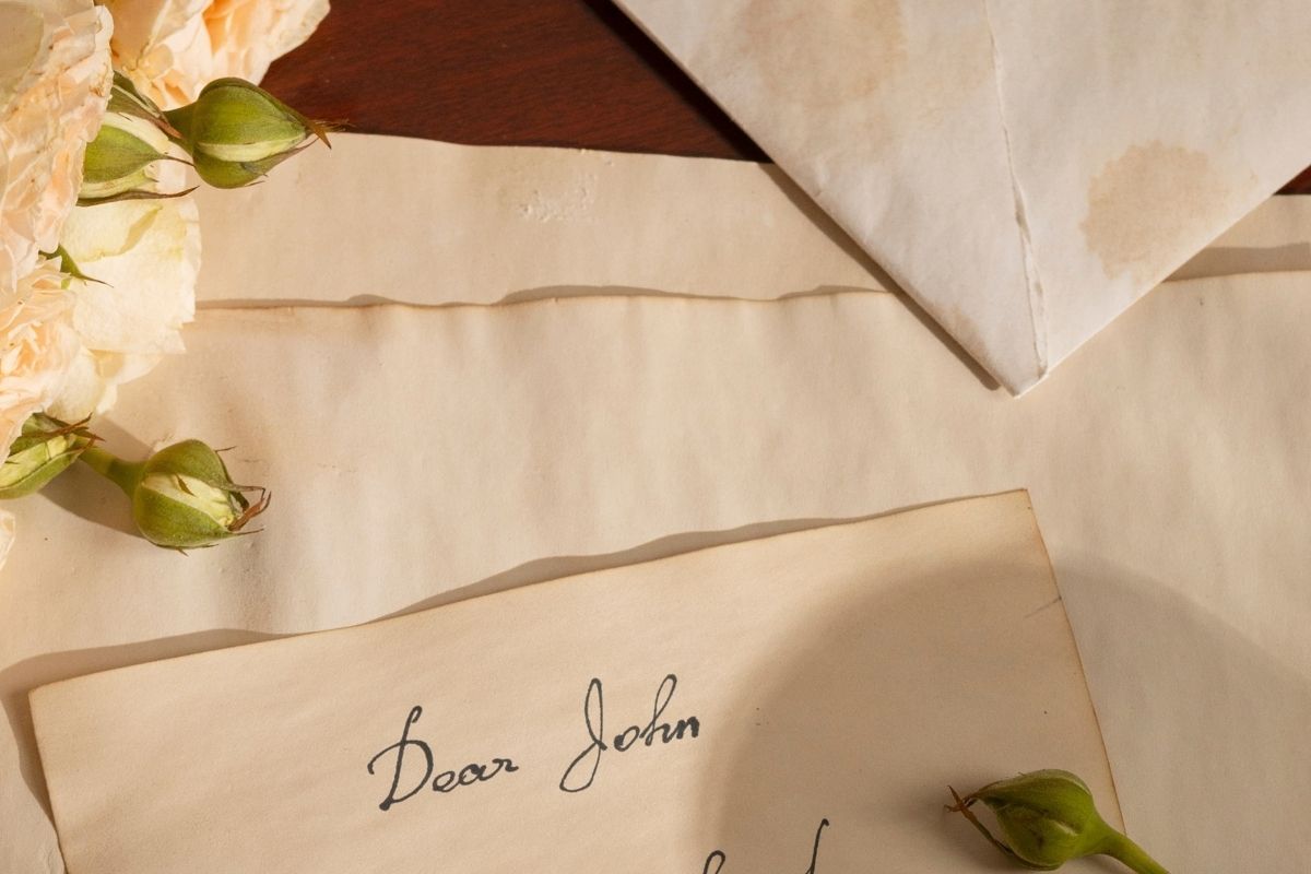 Handwritten letter and envelopes arranged with pale flowers on a wooden table.