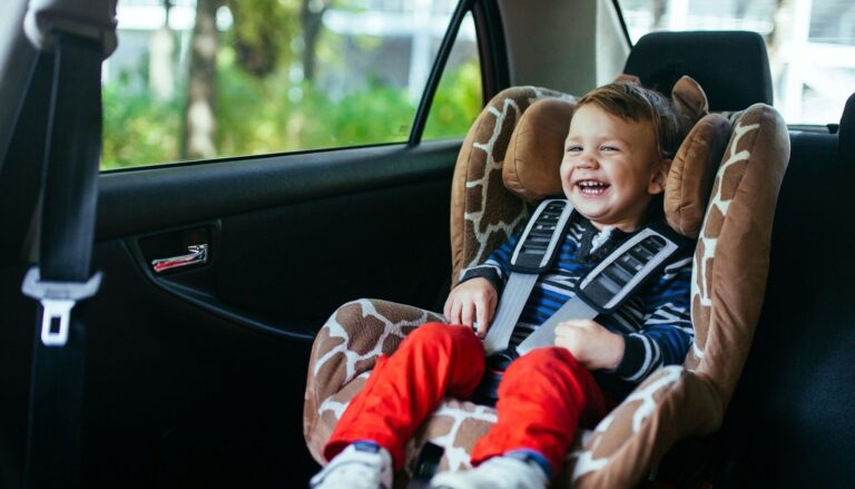 Smiling young child secured in a car seat in the back seat of a vehicle.
