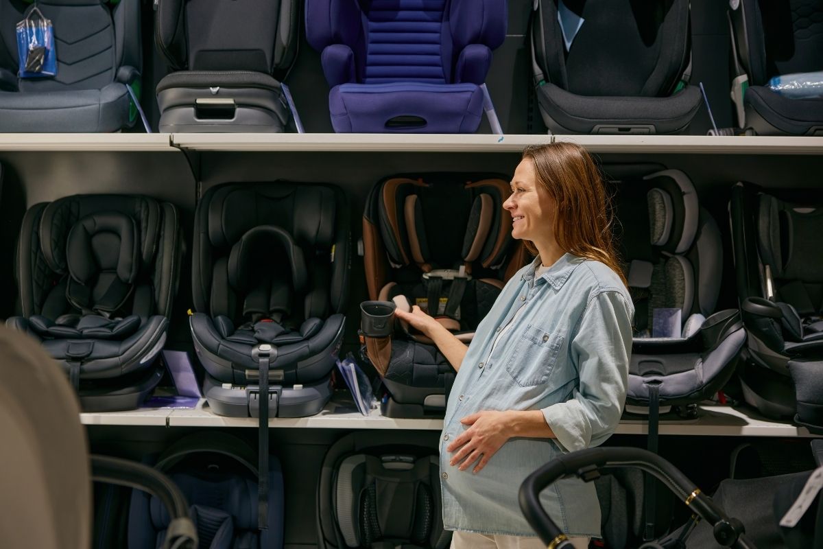 Pregnant woman shopping for a child car seat in a baby store.