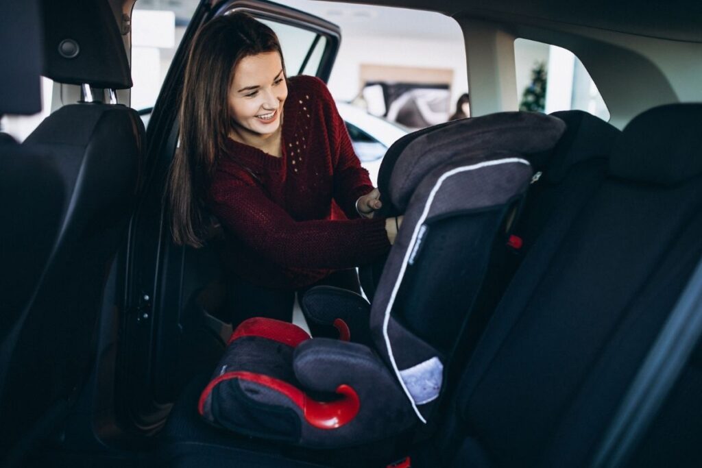 Woman adjusting a child car seat in the back seat of a vehicle.