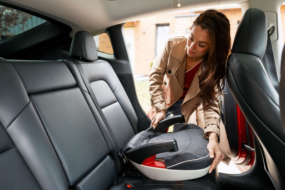 Woman installing a child booster seat in the back seat of a car.