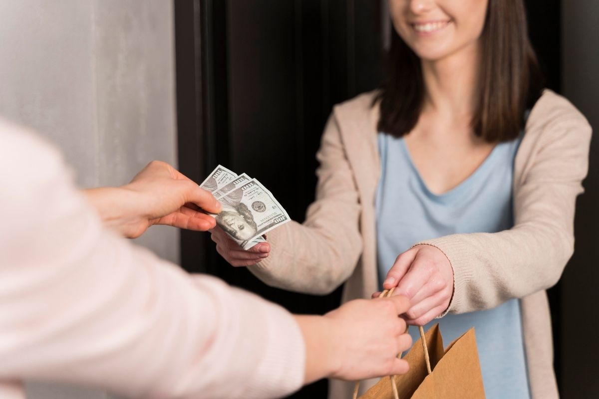 Woman receiving cash from another person while holding a gift bag at the door.