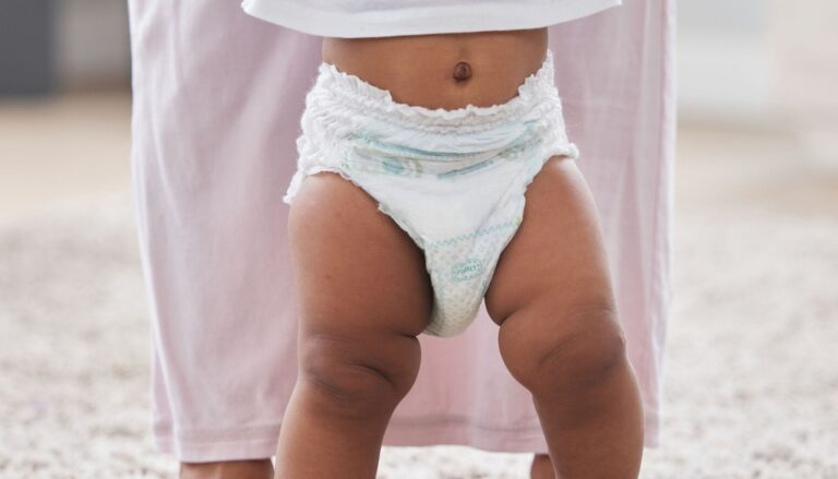 Toddler wearing a disposable pull-up while standing with an adult at home.