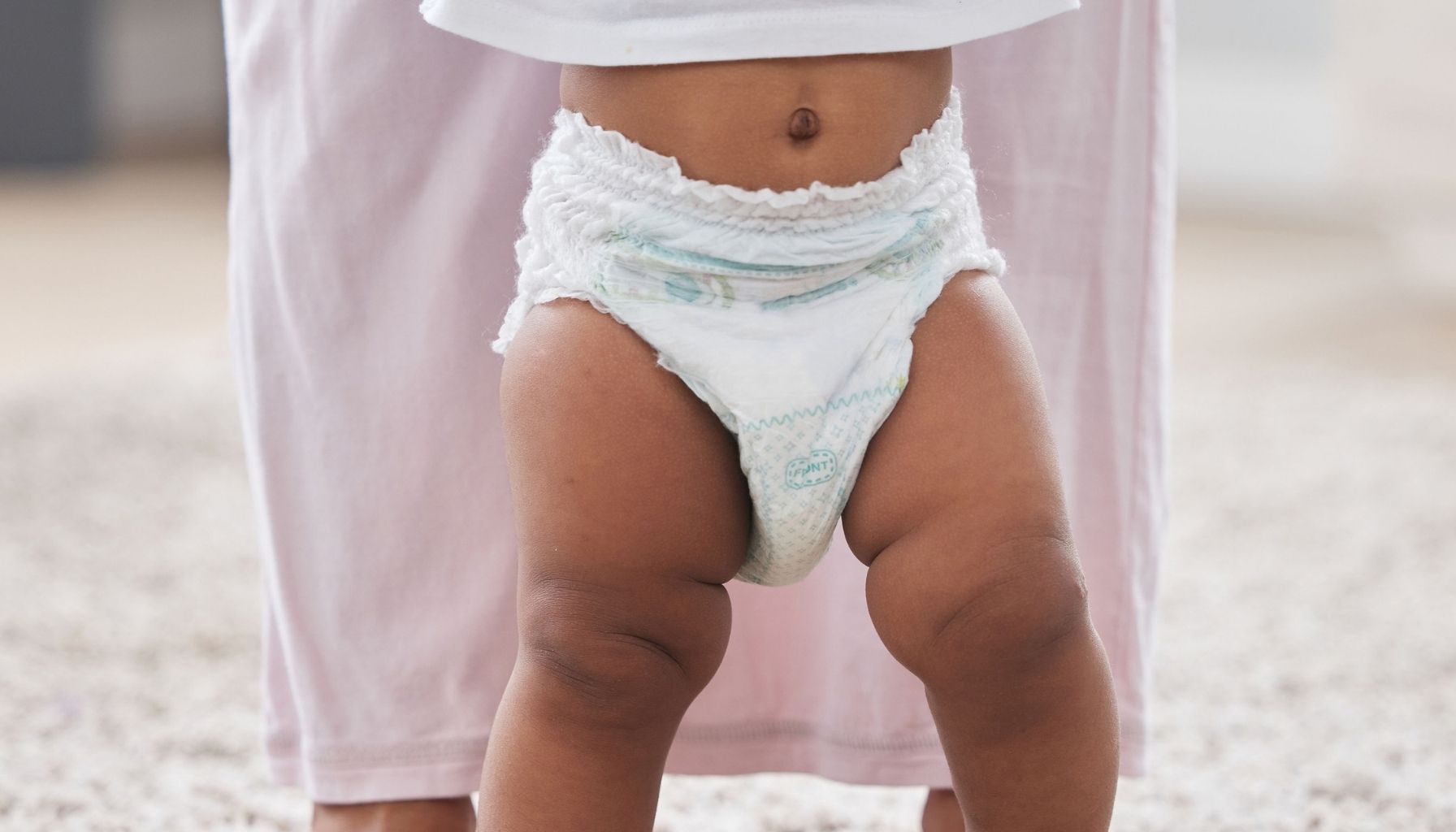 Toddler wearing a disposable pull-up while standing with an adult at home.