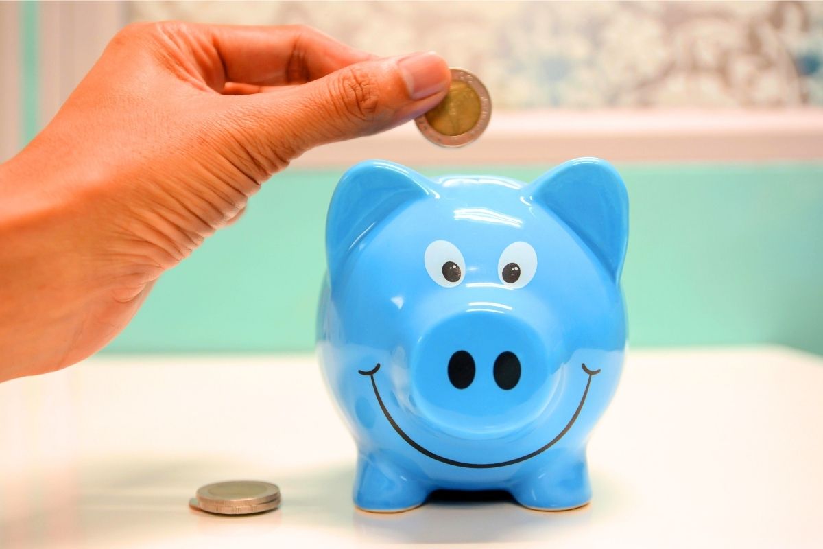 Hand dropping a coin into a blue piggy bank.