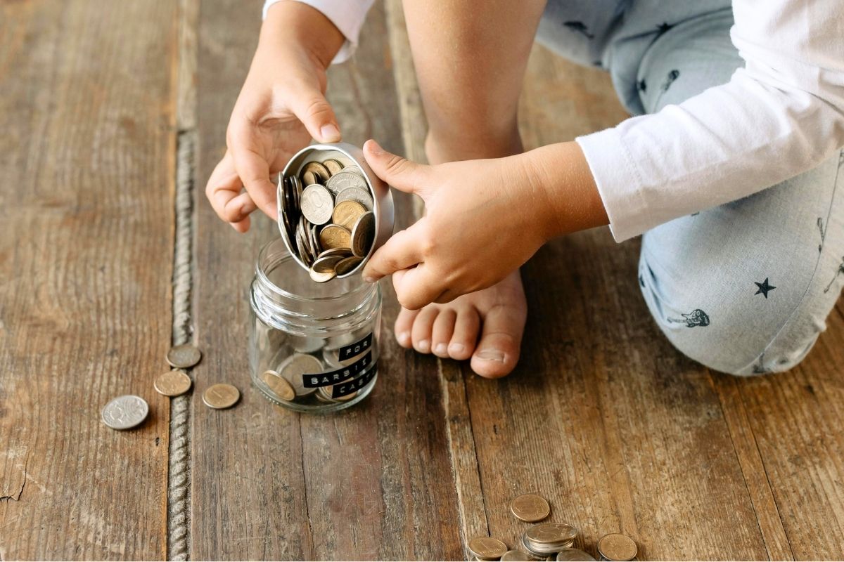 Children counting coins from a glass jar on a wooden floor.