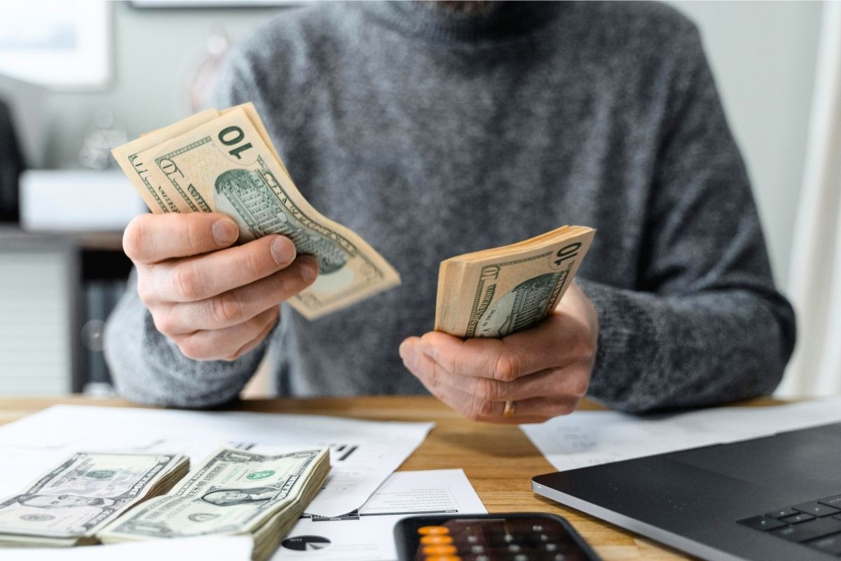 Person counting dollar bills while sitting at a desk.