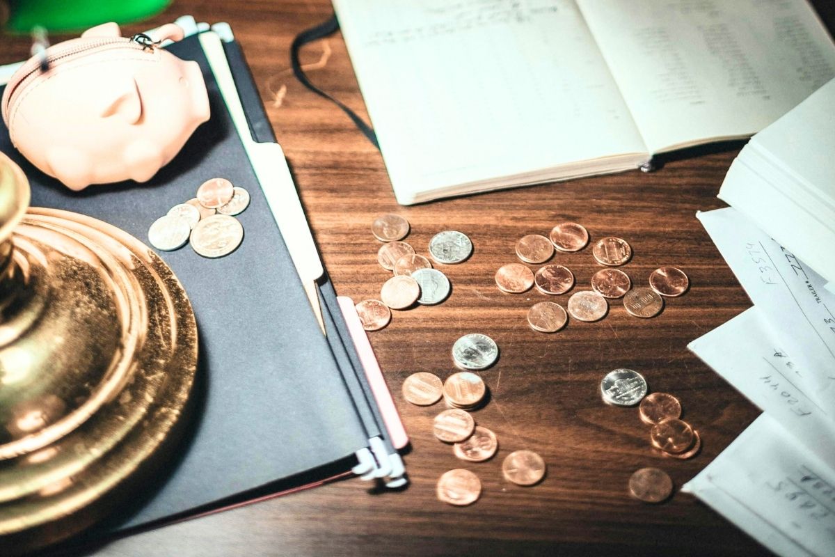 Coins spread across a desk next to a notebook and pen.
