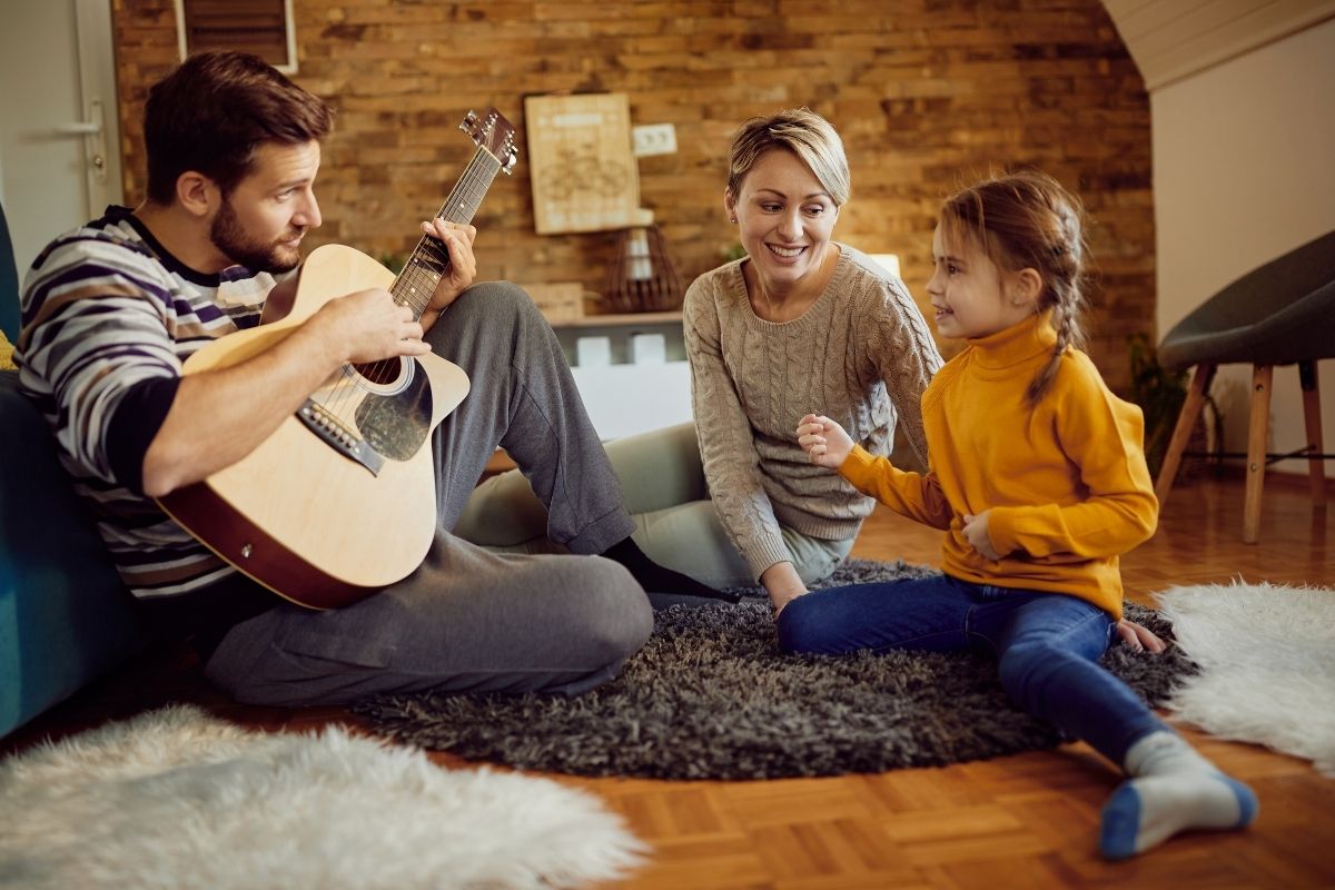 Father playing an acoustic guitar while a mother and daughter enjoy music together at home.