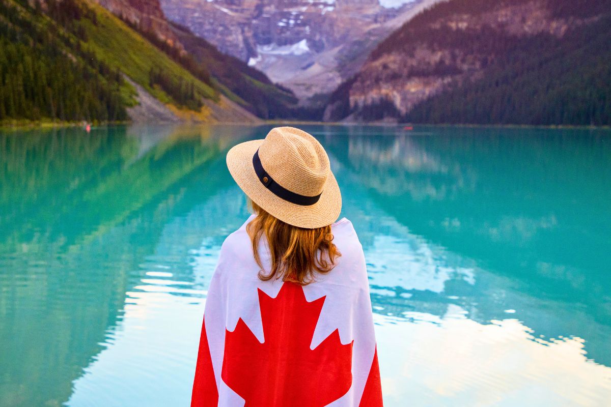Woman wrapped in Canadian flag beside turquoise mountain lake in Canada.
