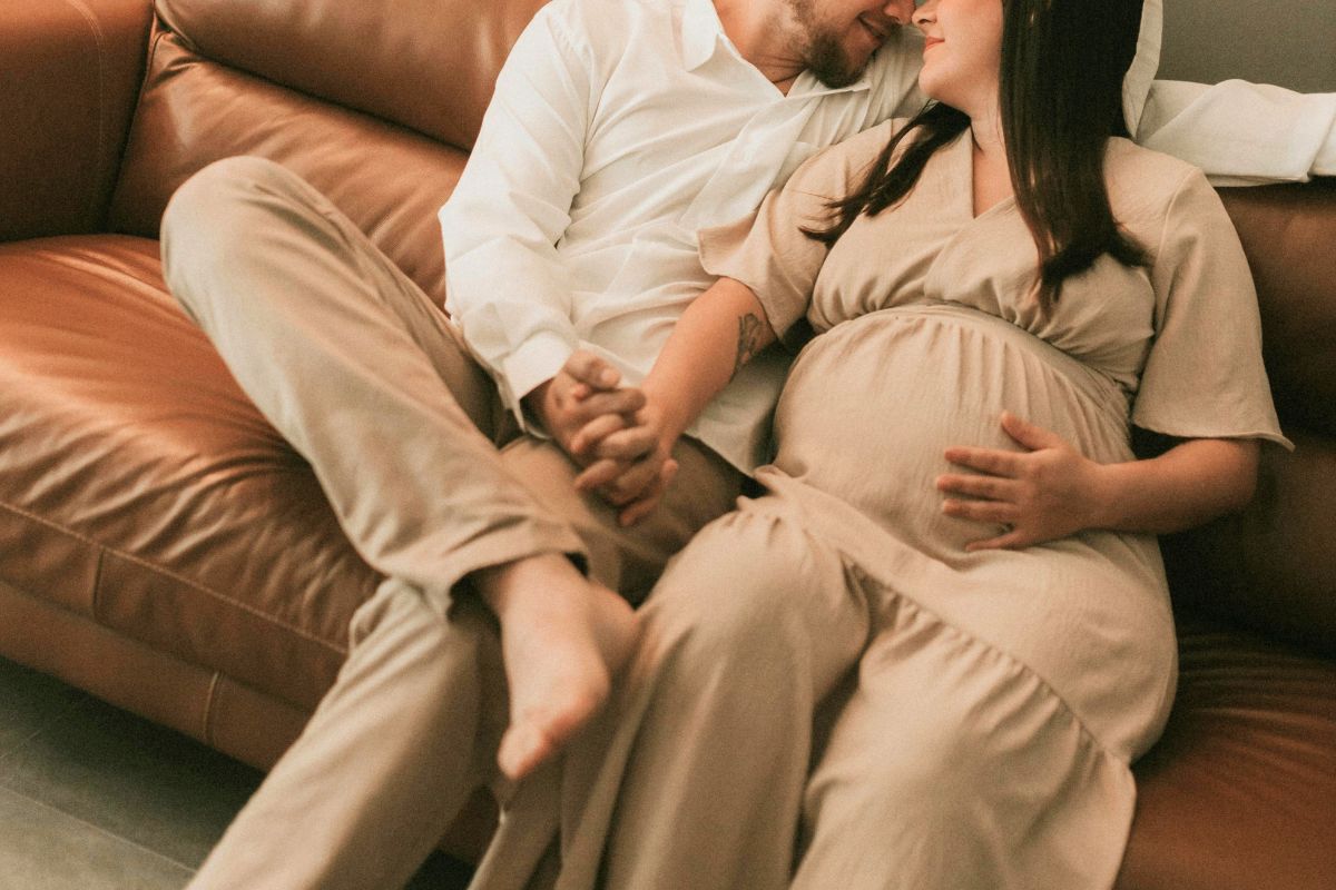 Pregnant couple relaxing together on a couch while planning a peaceful all-inclusive babymoon before baby arrives.