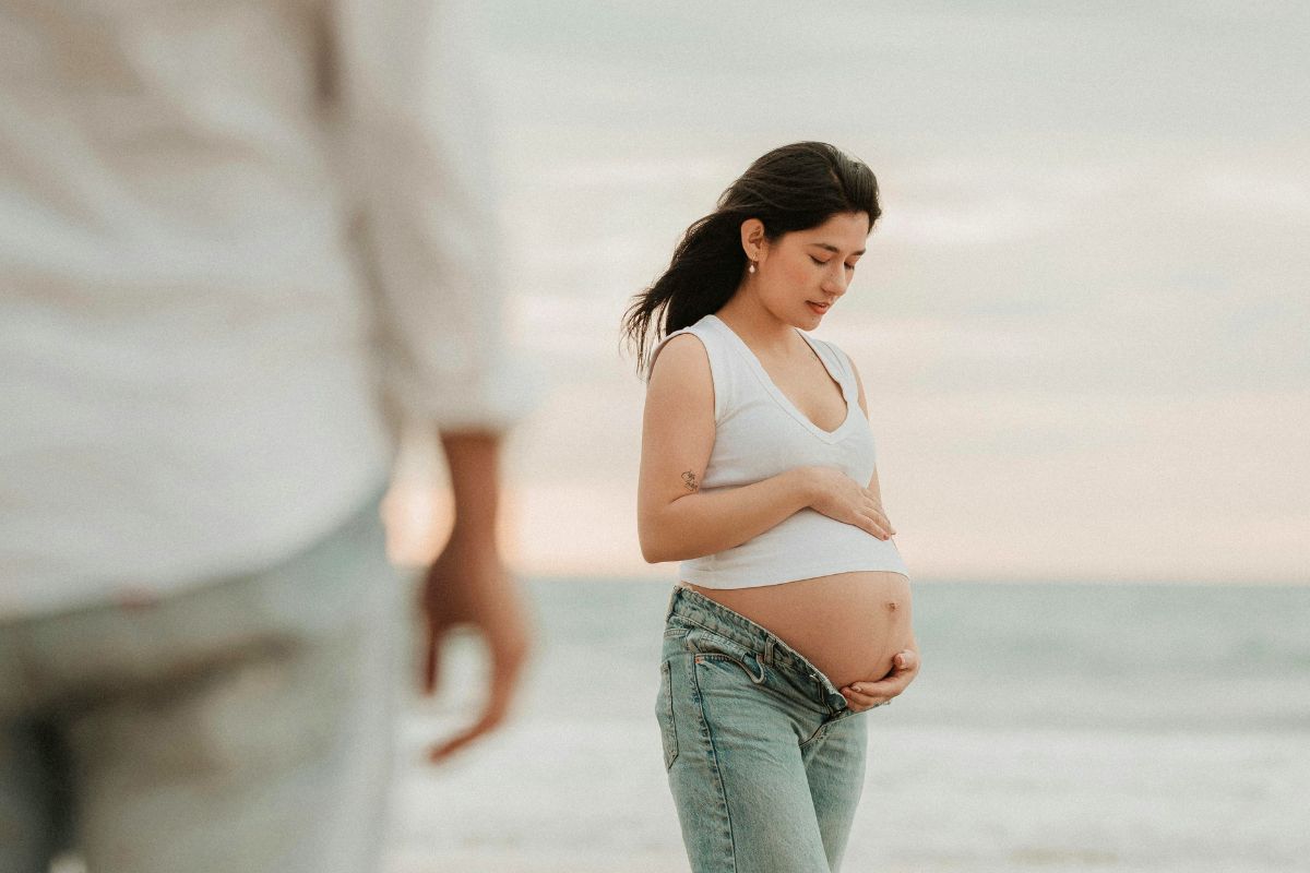 Pregnant woman standing by the beach during a relaxing babymoon getaway with the ocean in the background.