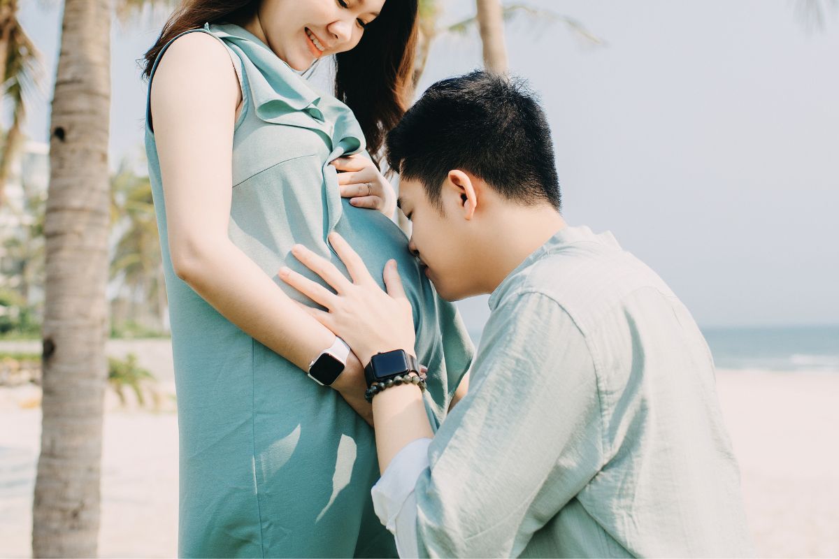 Expecting couple enjoying a quiet beach moment during an all-inclusive babymoon vacation before baby arrives.