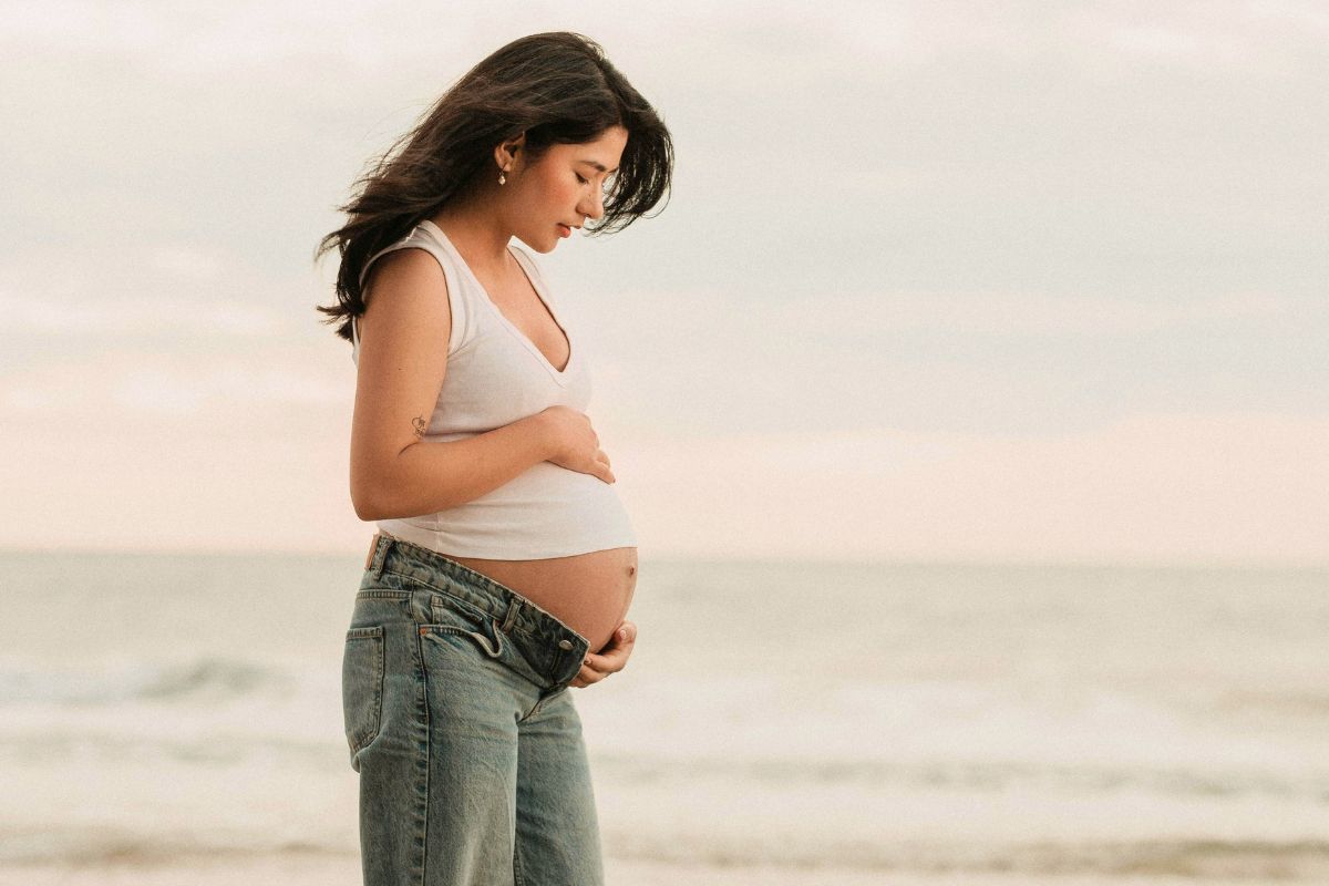 Pregnant woman standing by the beach during a relaxing babymoon getaway, enjoying a peaceful moment before welcoming her baby.