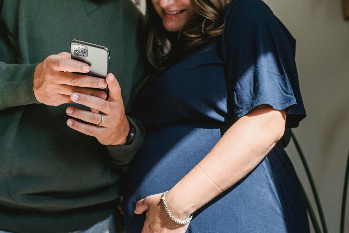 Expecting couple looking at a phone while planning their babymoon and preparing for their growing family.