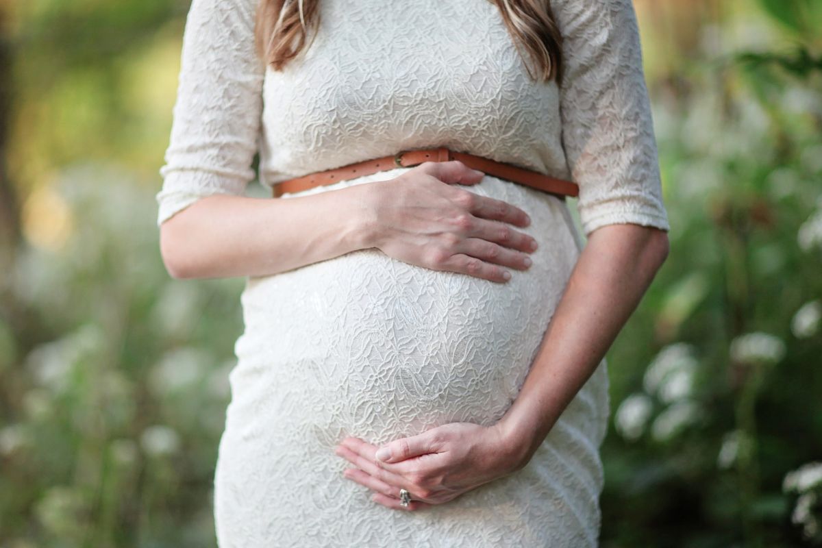 Pregnant woman gently holding her baby bump outdoors, celebrating pregnancy and anticipating motherhood.