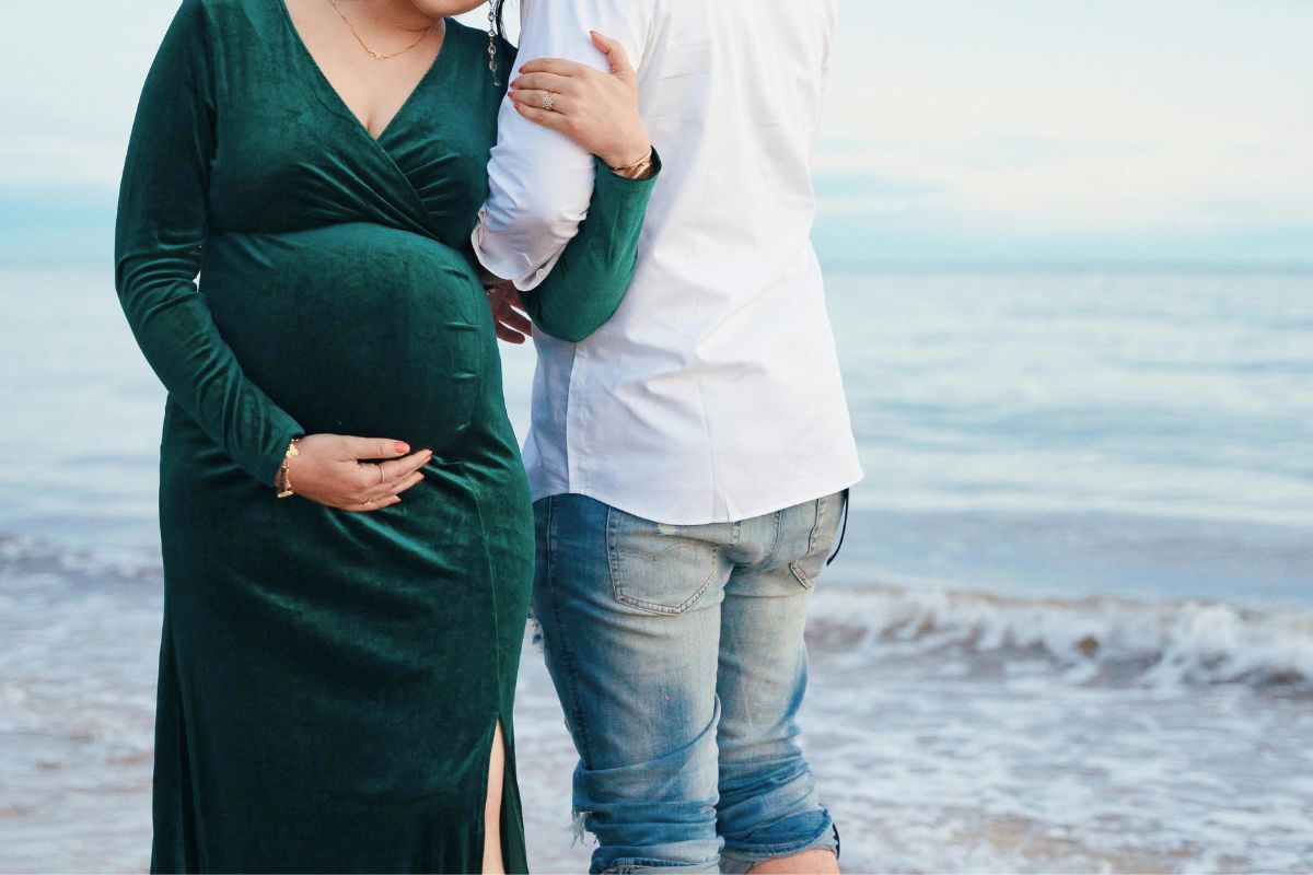 Expecting couple enjoying a peaceful beach babymoon, spending quality time together before becoming parents.