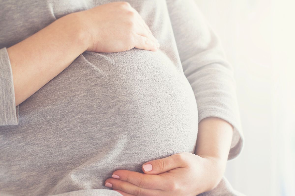Close-up of a pregnant woman holding her baby bump, representing pregnancy, anticipation, and pre-baby travel planning.