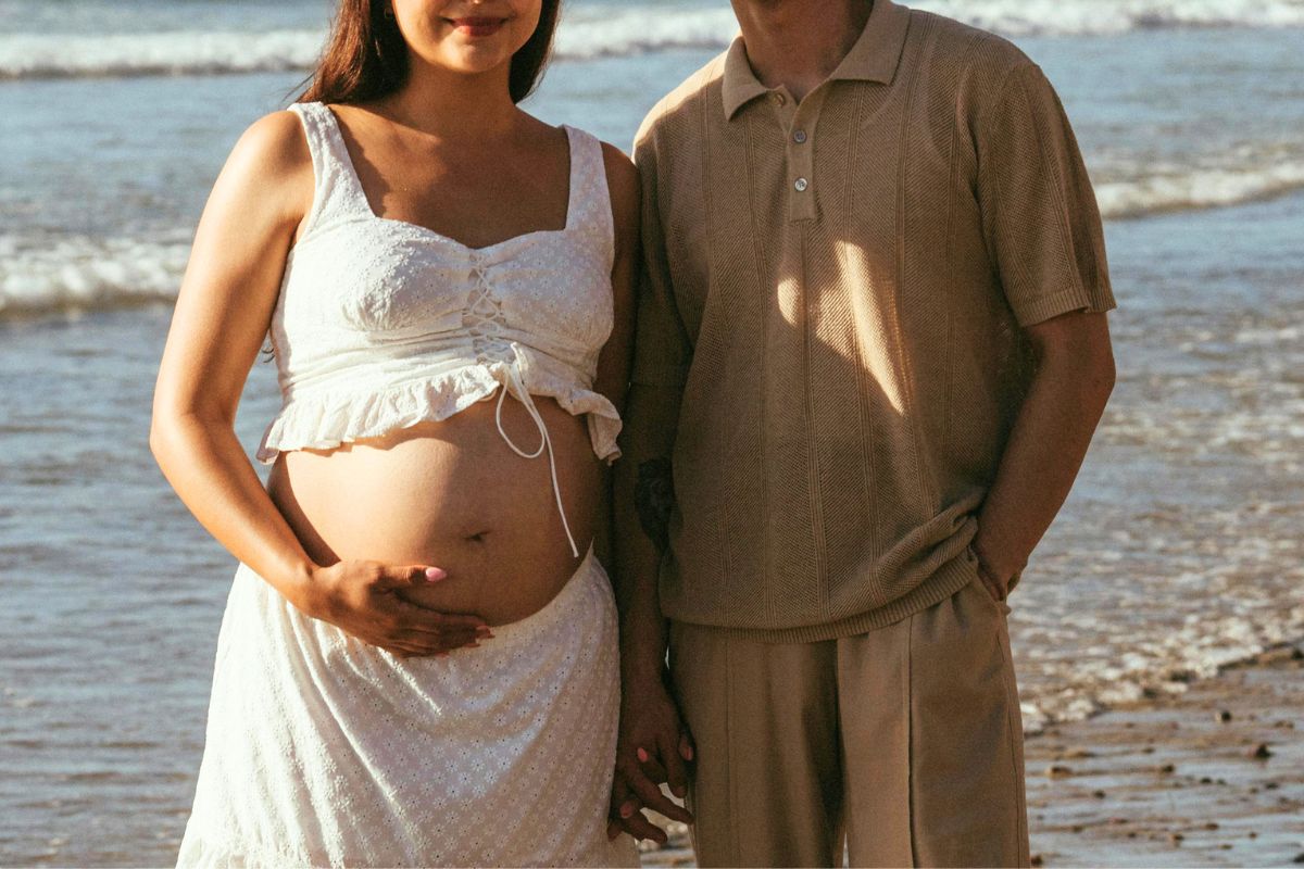 Expecting couple standing together on the beach during a babymoon vacation, enjoying a relaxing getaway before their baby arrives.