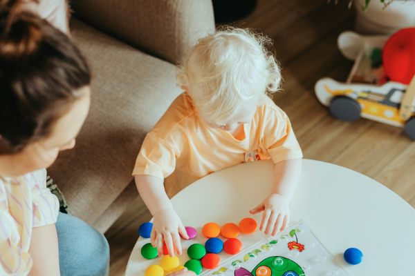 Parent and toddler playing with colorful toys at home during daily routine time.