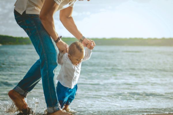 Parent helping a child walk along the beach, representing family bonding time.