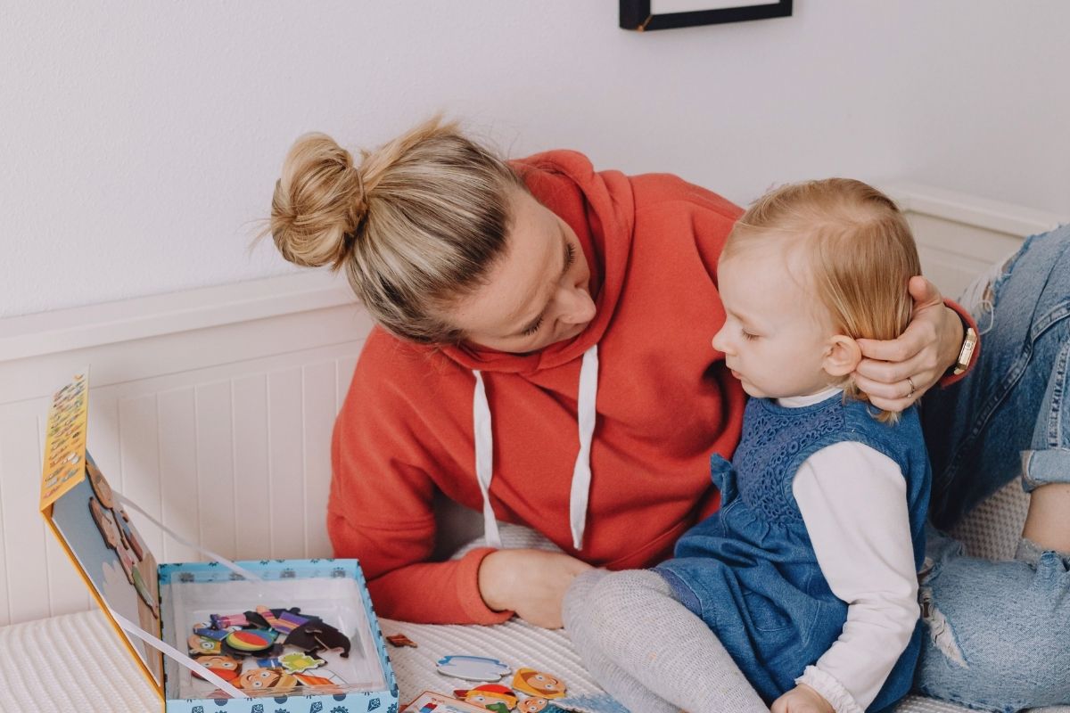 Woman sitting on a bed with toddler, looking at a picture cards and playing tohether