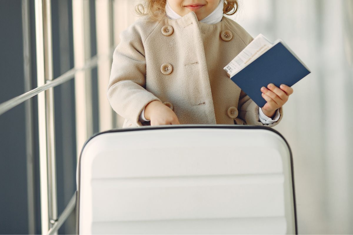 Child holding passport and suitcase at airport, representing family travel preparation when flying with kids in Canada.