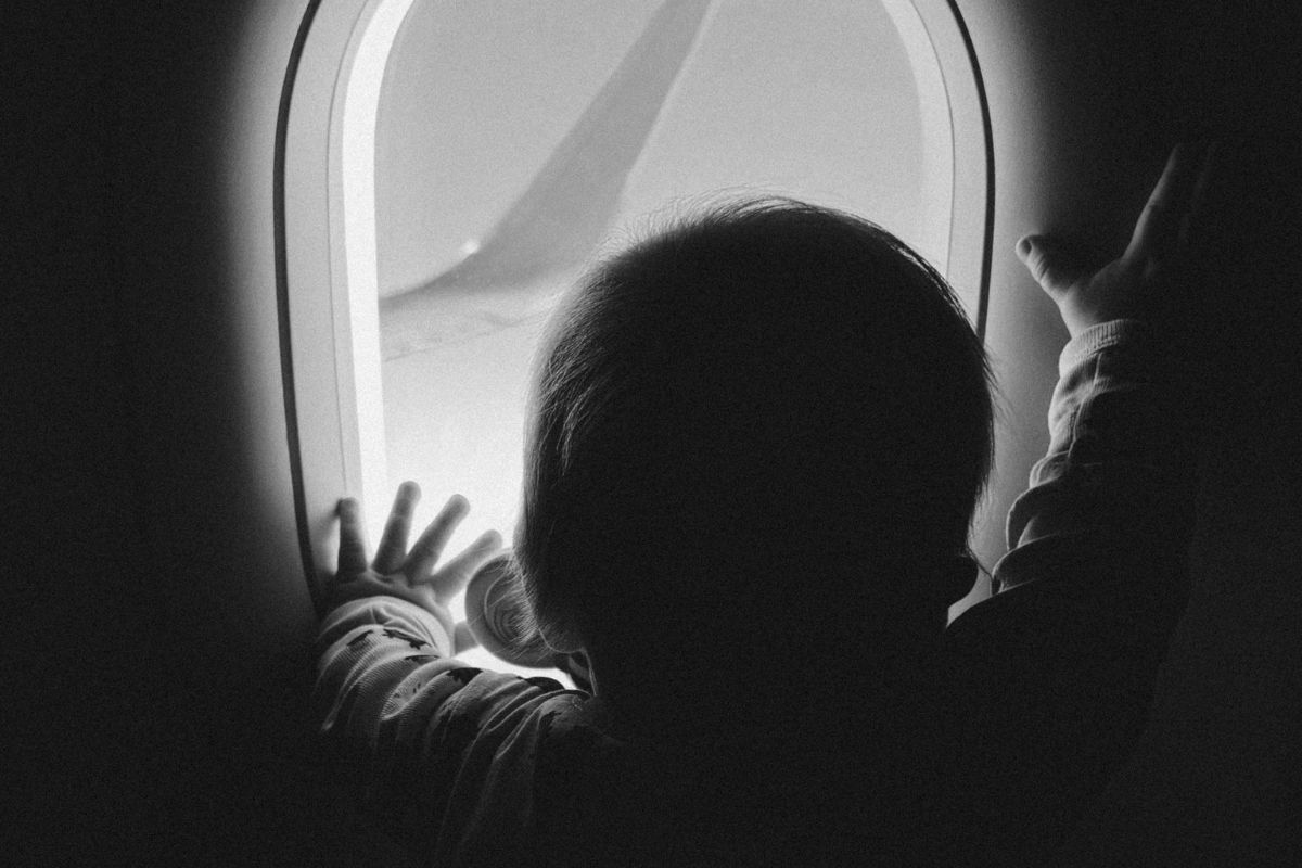 Child looking out airplane window during flight, capturing a quiet moment while traveling with kids in Canada.
