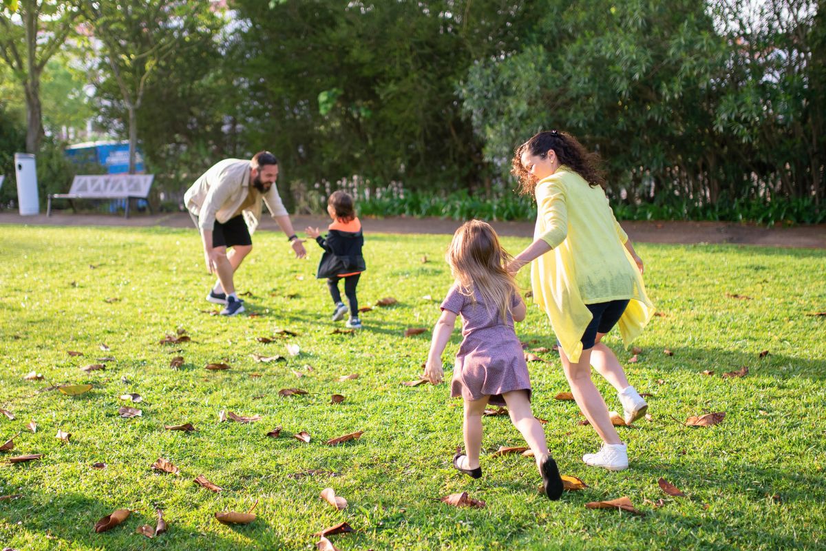Parents and young children running through a grassy park during a family-friendly outdoor trip.