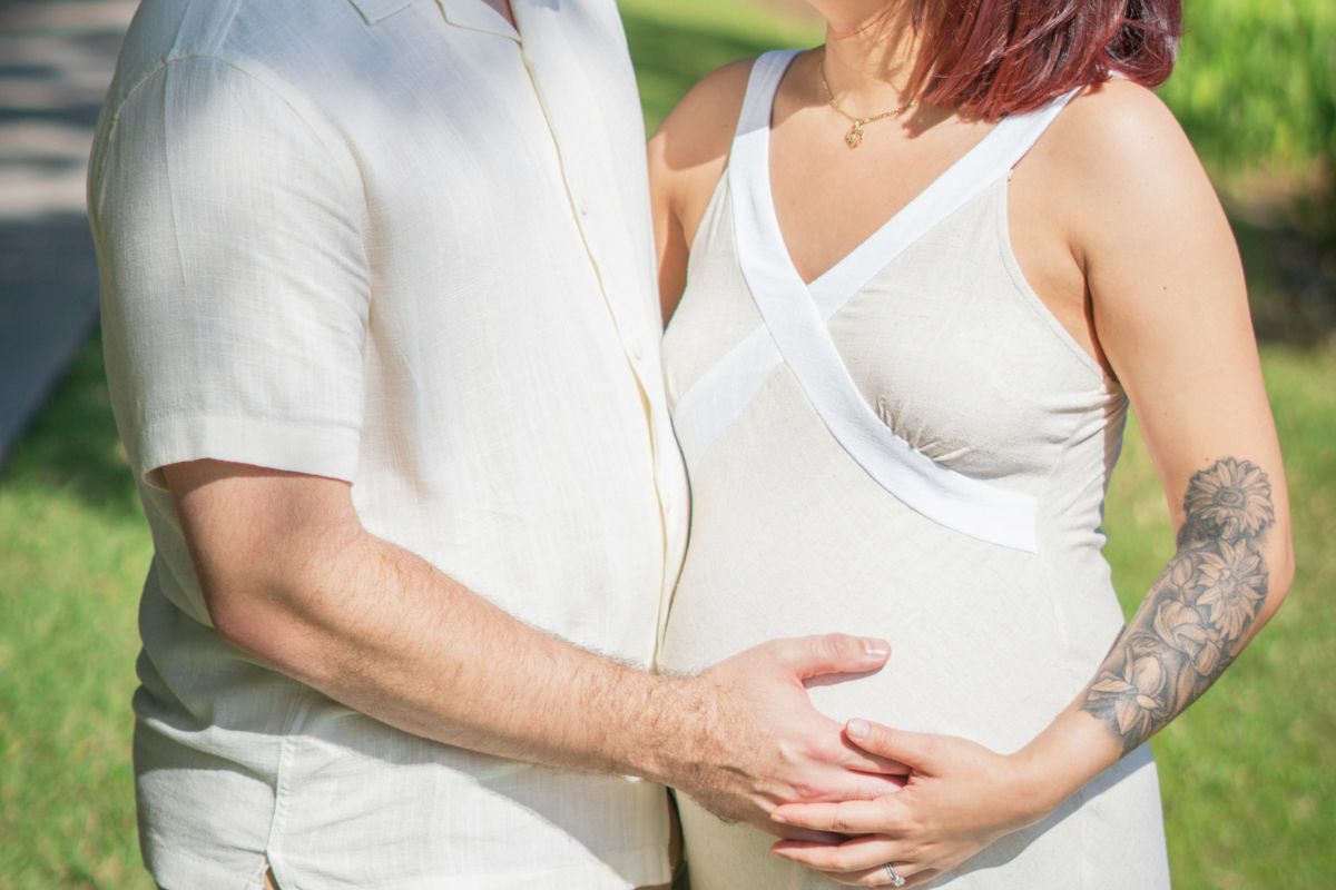 Pregnant couple holding baby bump outdoors while planning the best time for a babymoon.