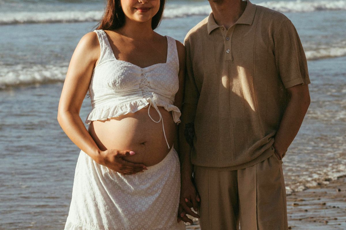 Expecting couple at the beach enjoying a peaceful babymoon trip during pregnancy.