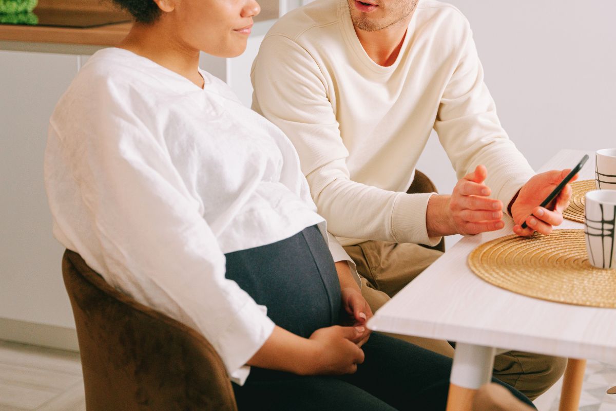 Pregnant couple sitting at home and planning when to take a babymoon.