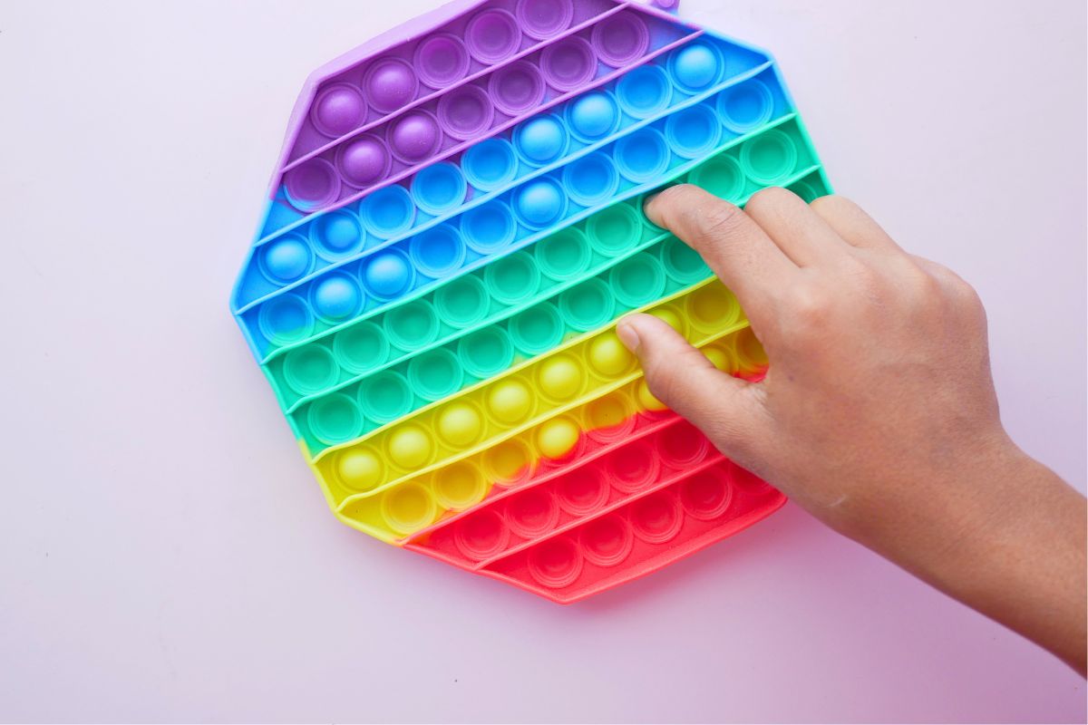 Child using a rainbow pop-it fidget toy, a calming sensory toy for toddlers during meals.