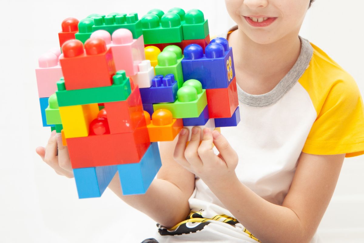 Child holding colorful building blocks toy, keeping hands busy during playtime at the table.