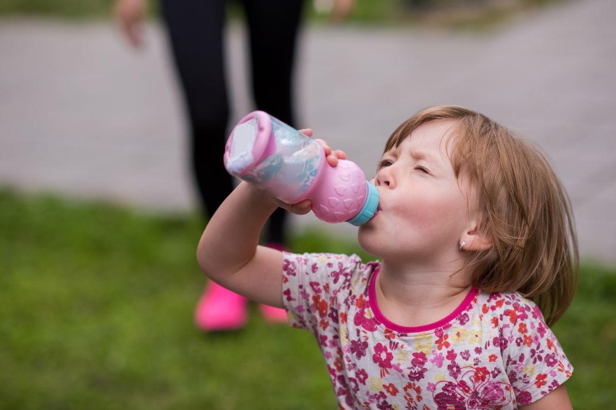Toddler drinking from a pink water bottle while playing outdoors.