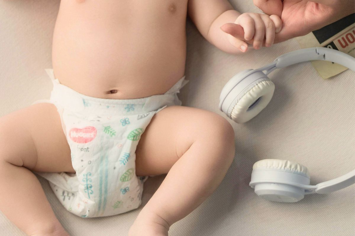 Baby wearing a clean diaper with headphones nearby, showing essentials for diaper changes during flights.