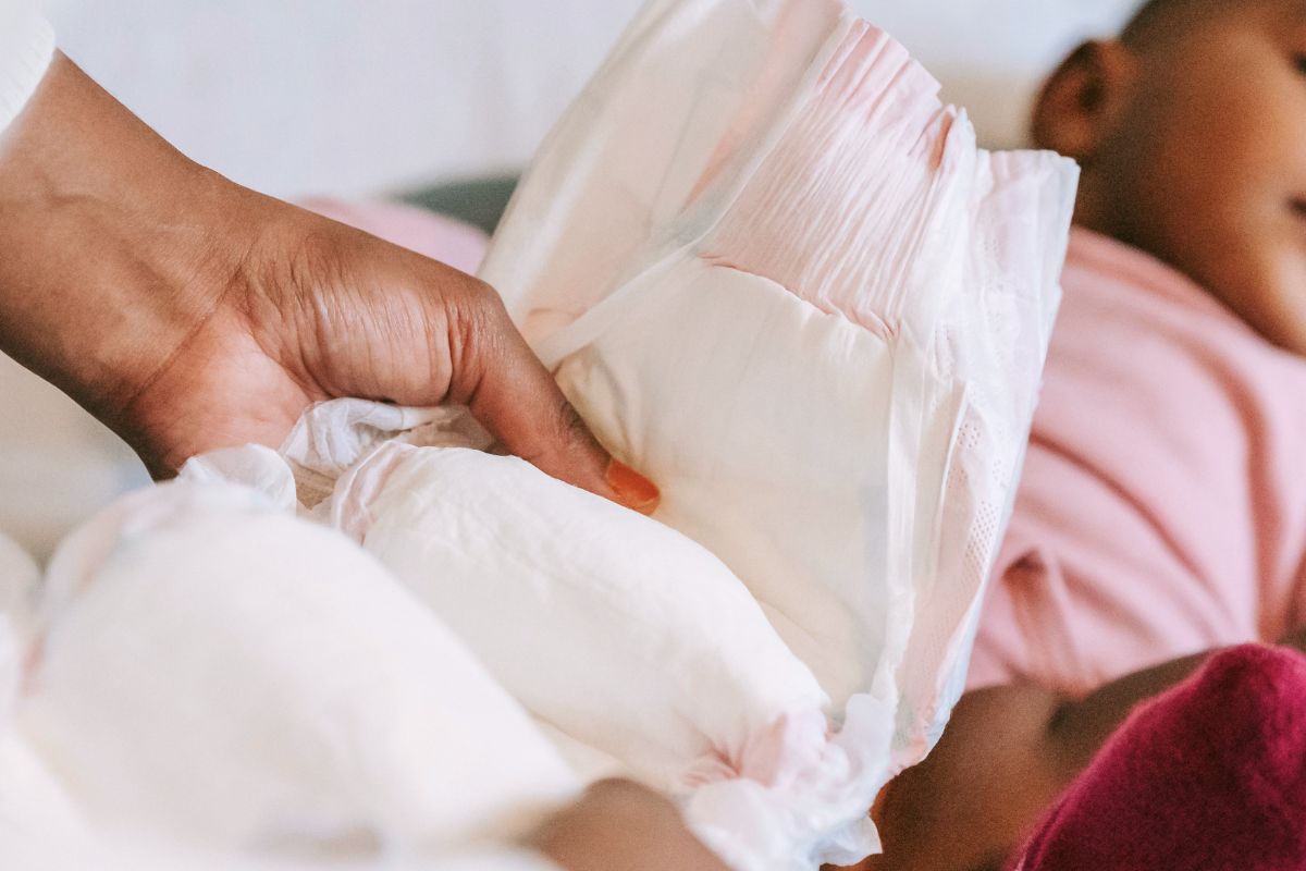 Parent holding a fresh diaper near a baby, preparing for a diaper change during travel.