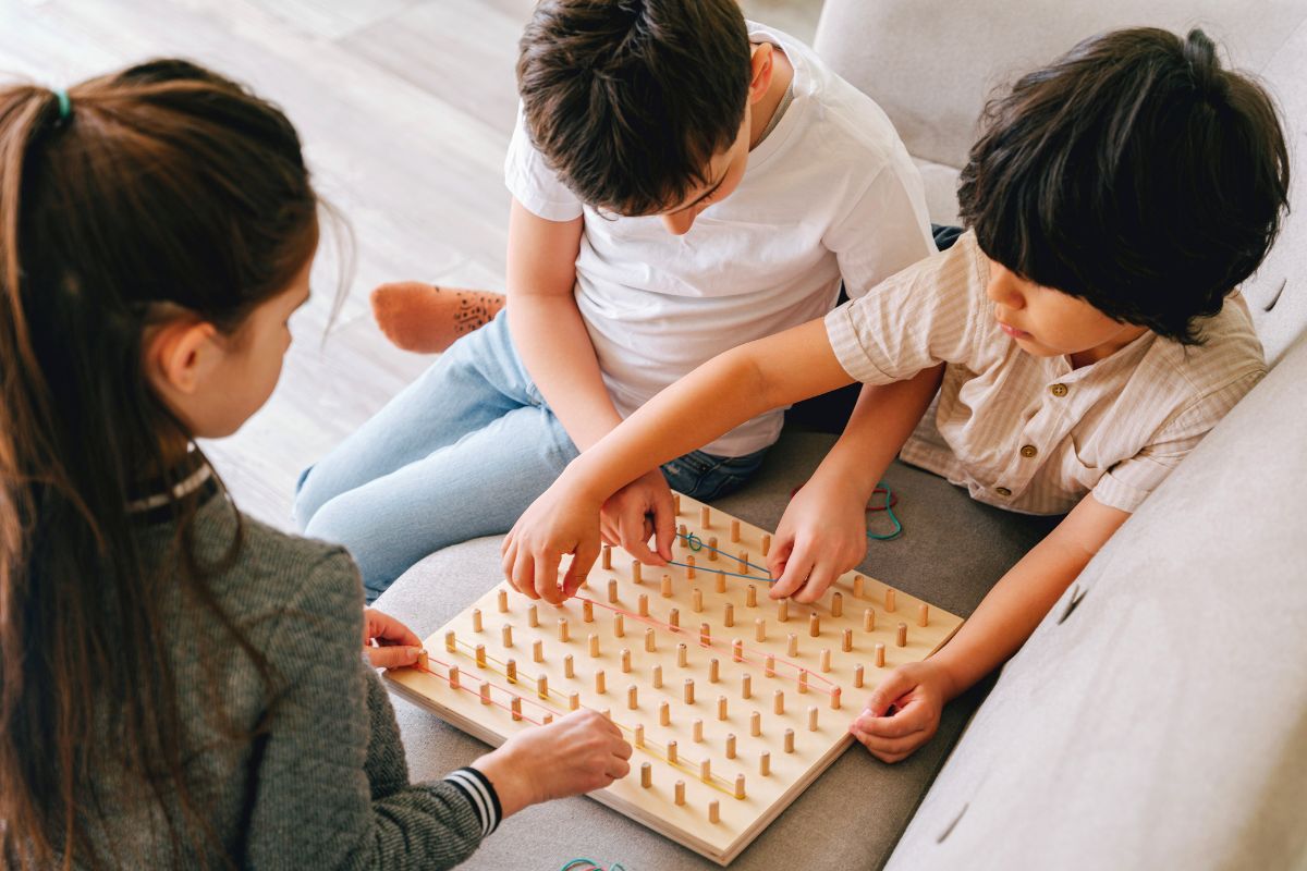 Three children working together on a wooden pegboard game during an indoor sibling activity.