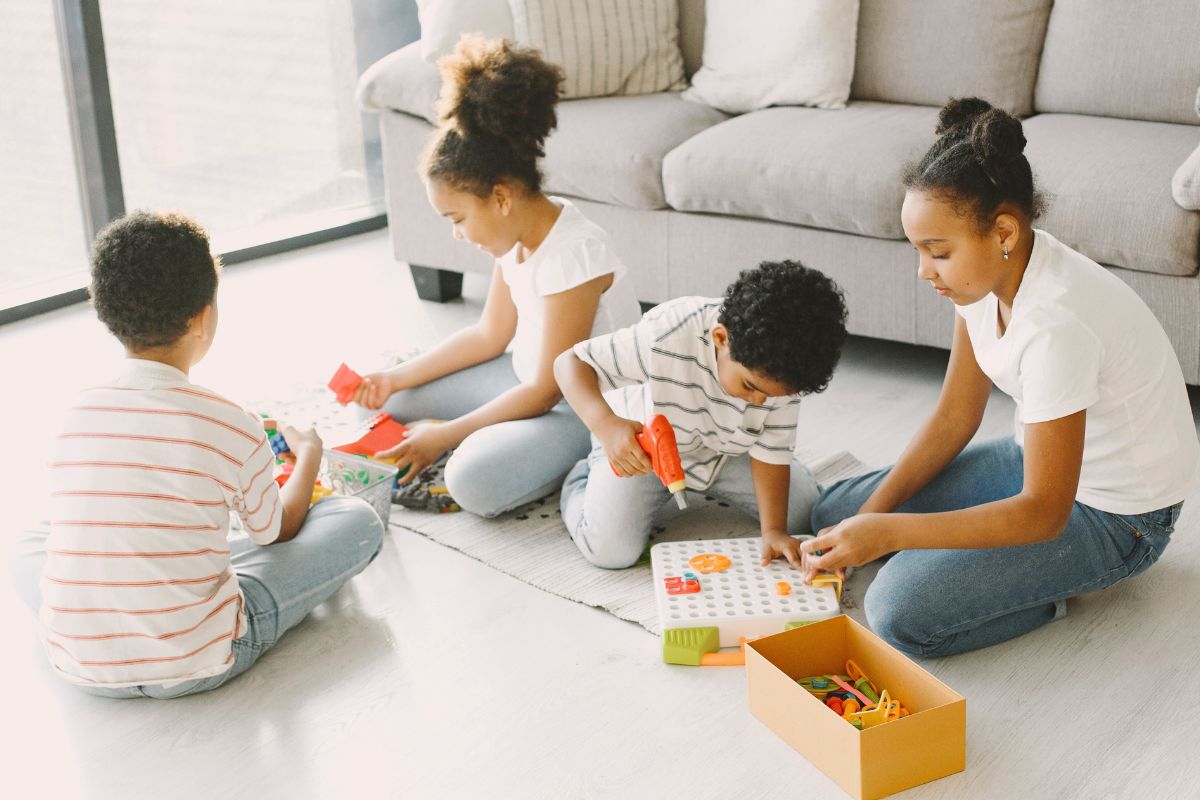 Four children sitting on the floor and creating a hands-on craft project together at home.