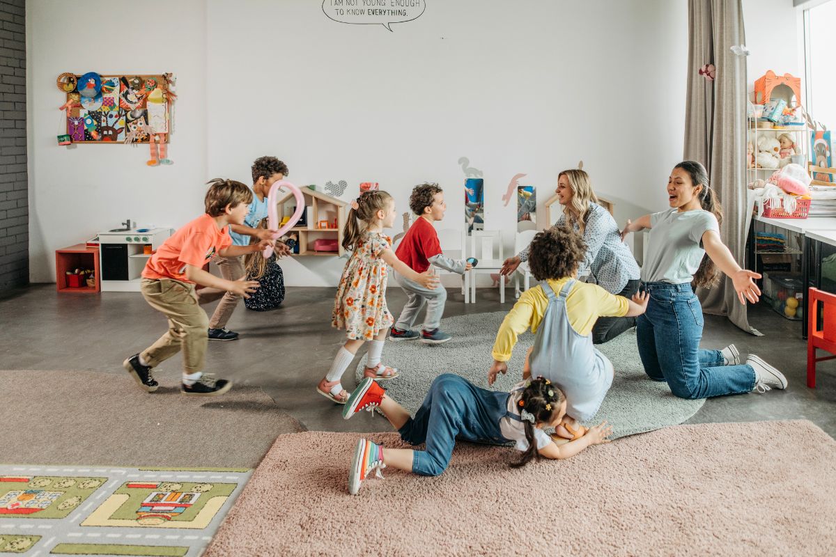 Children playing with daycare teachers during a classroom activity, showing staff warmth and social interaction.
