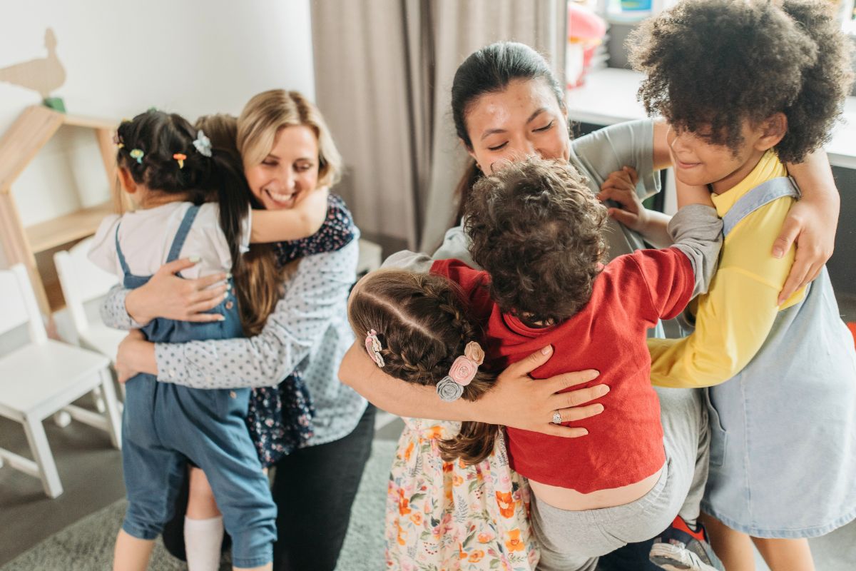 Daycare teachers comforting children with hugs, showing a caring and supportive classroom environment.