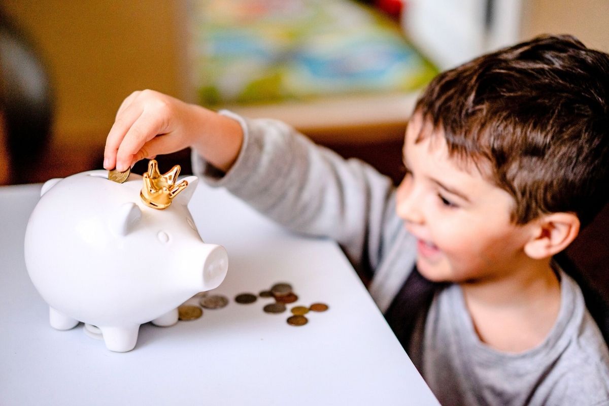 Little boy adding cash to a piggy bank.