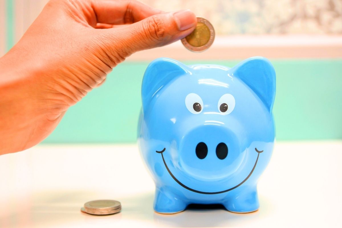 Blue piggy bank with cash about to go in it.