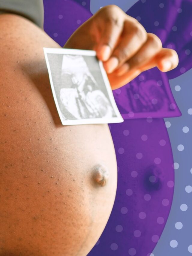 Pregnant woman holding a small ultrasound photo against her belly, showing early baby imaging.